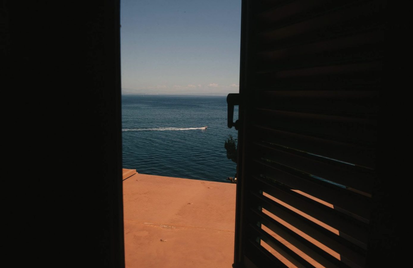 View of the sea through open shutters onto a terracotta terrace