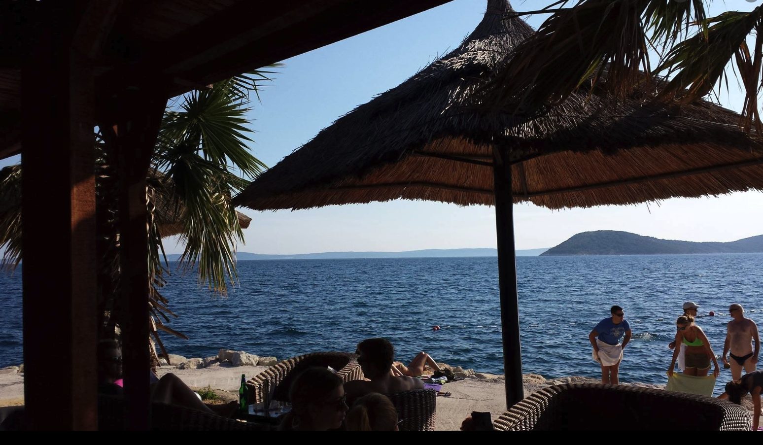 View of the Adriatic coastline from beneath a thatched umbrella at a beach club