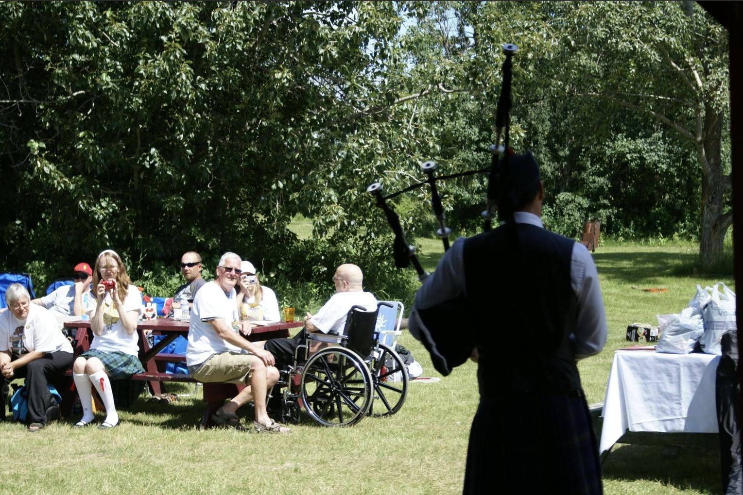 Sean Rathwell piping for guests seated at picnic tables outdoors