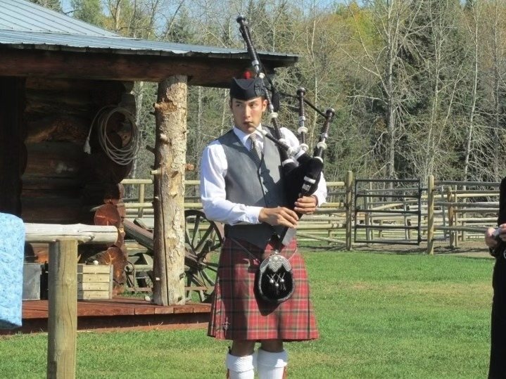 Sean Rathwell piping at a countryside venue in red tartan Highland dress