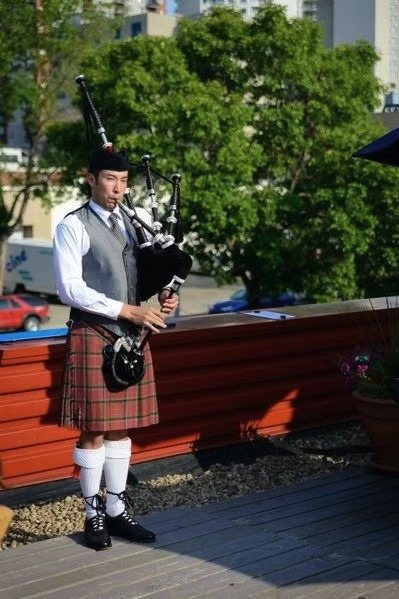 Sean Rathwell piping on a rooftop terrace in red tartan Highland dress