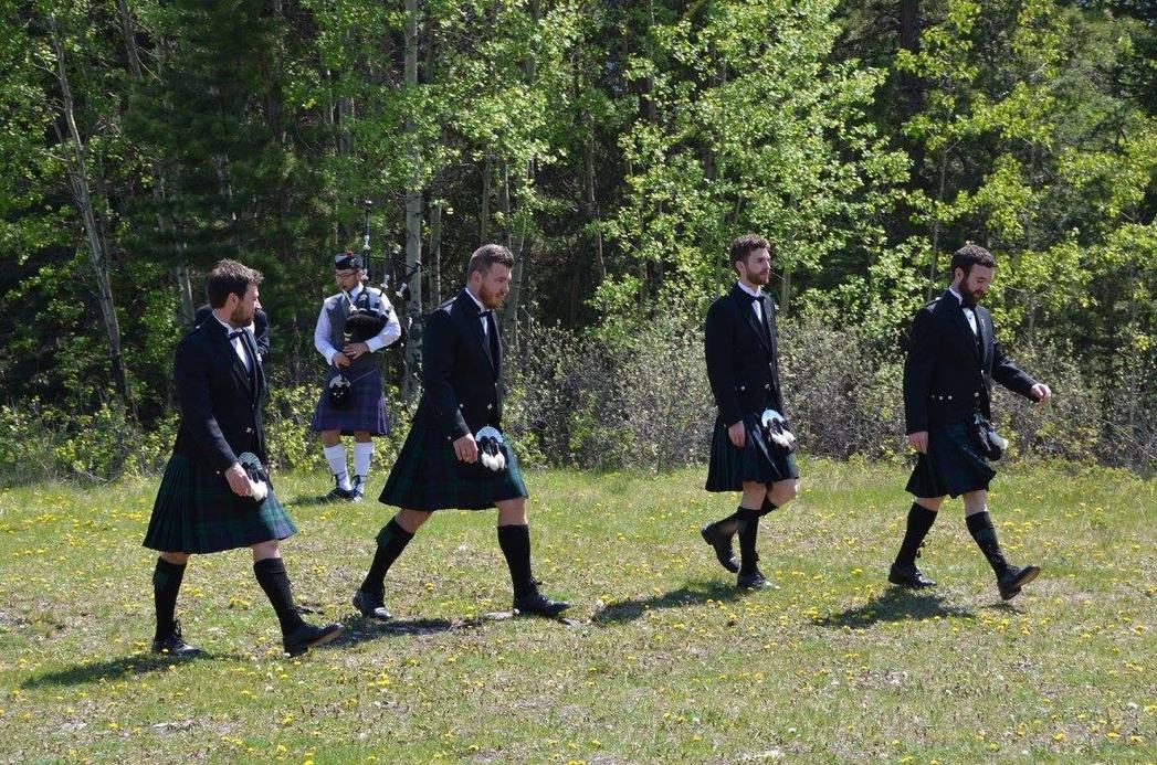 Sean Rathwell piping as groomsmen process across a meadow at a real wedding